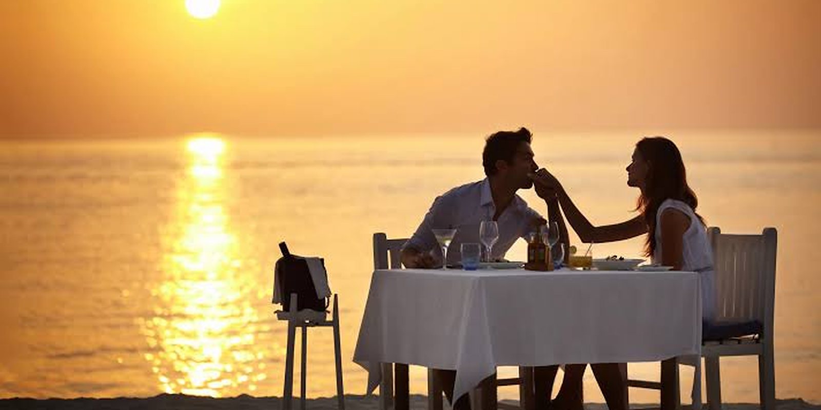 Casal jantando à beira-mar durante o pôr do sol