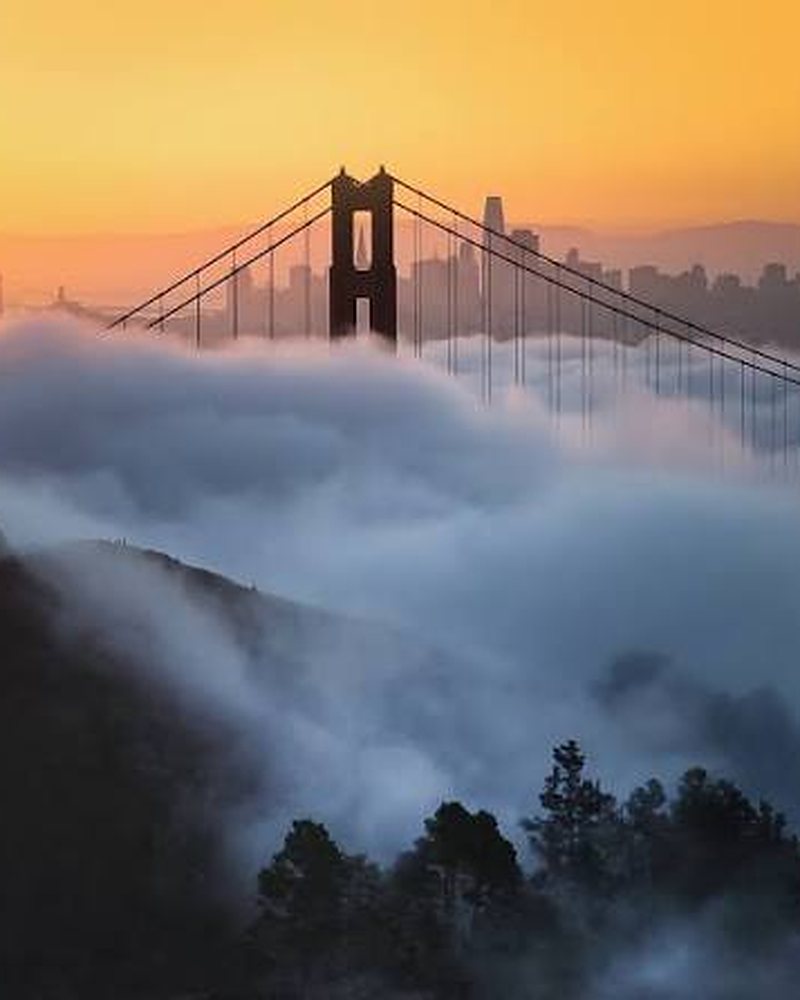 Ponte Golden Gate emergindo da neblina ao entardecer, com o skyline de São Francisco ao fundo